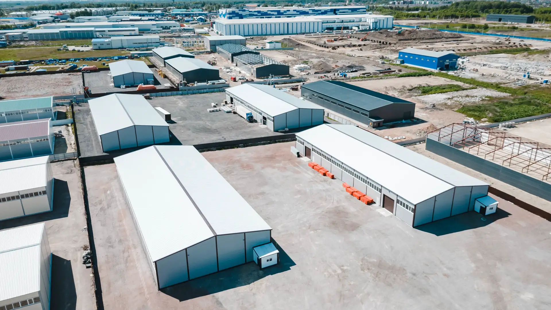 Фотография хорошо убраной дороги в Технопарке Фёдоровское с проезжающими по ней двумя большими ярко оранжевыми фурами. Фото снято зимой с квадрокоптера